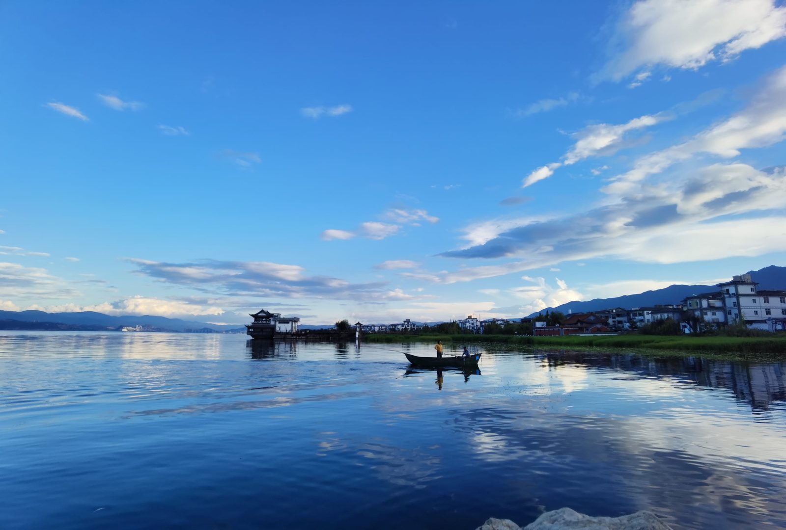 Erhai Lake at dusk with lakeside pavilions and a small boat