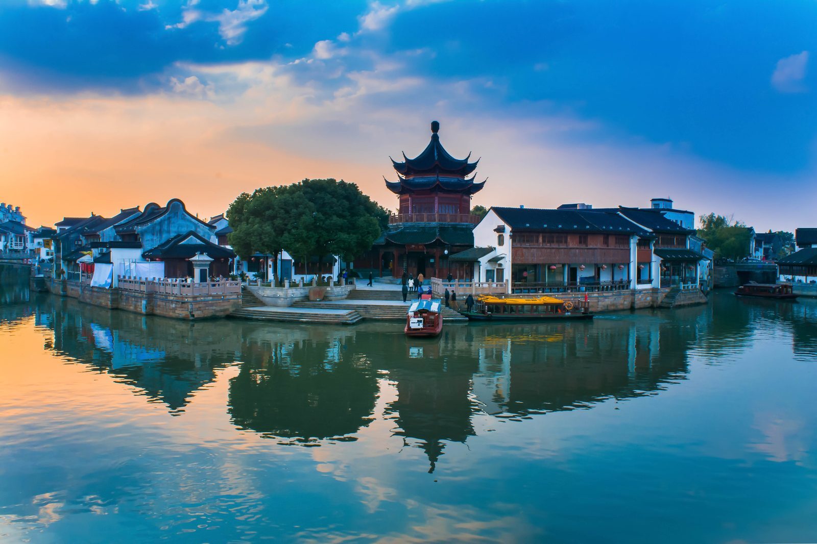 Upturned eaves of a water-town pavilion and sightseeing boats at dusk