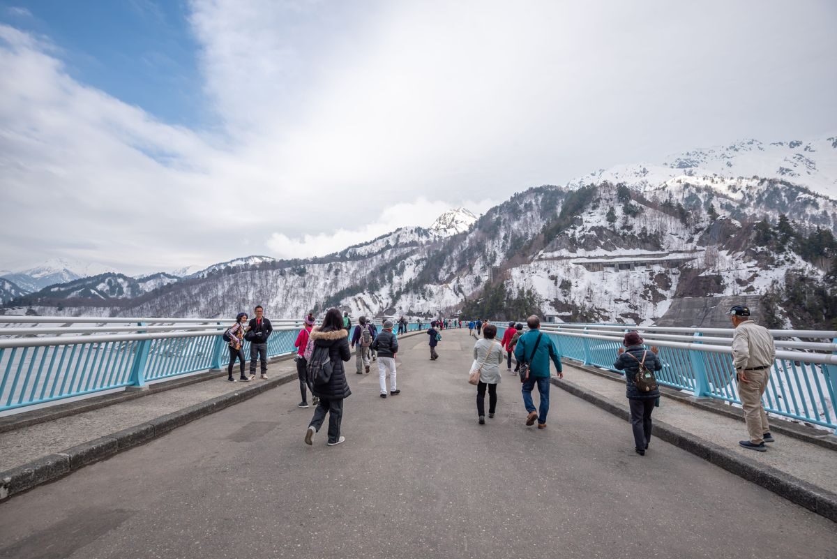 Walkway along the crest of Kurobe Dam with snow-streaked mountains behind